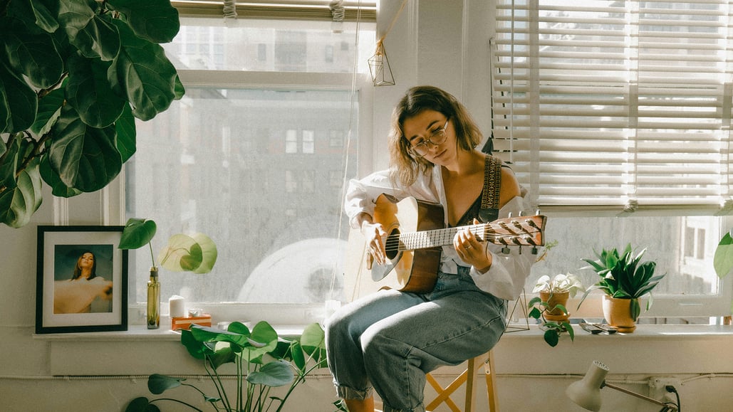 A woman in white shirt and blue denim jeans playing a cover song on a guitar, wondering how to get a mechanical license for cover song.