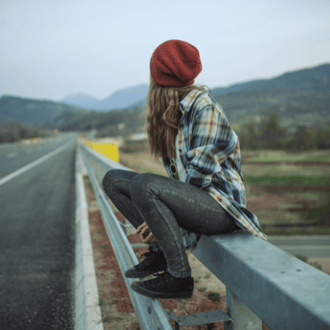 Young woman sitting on a fence looking at the open road